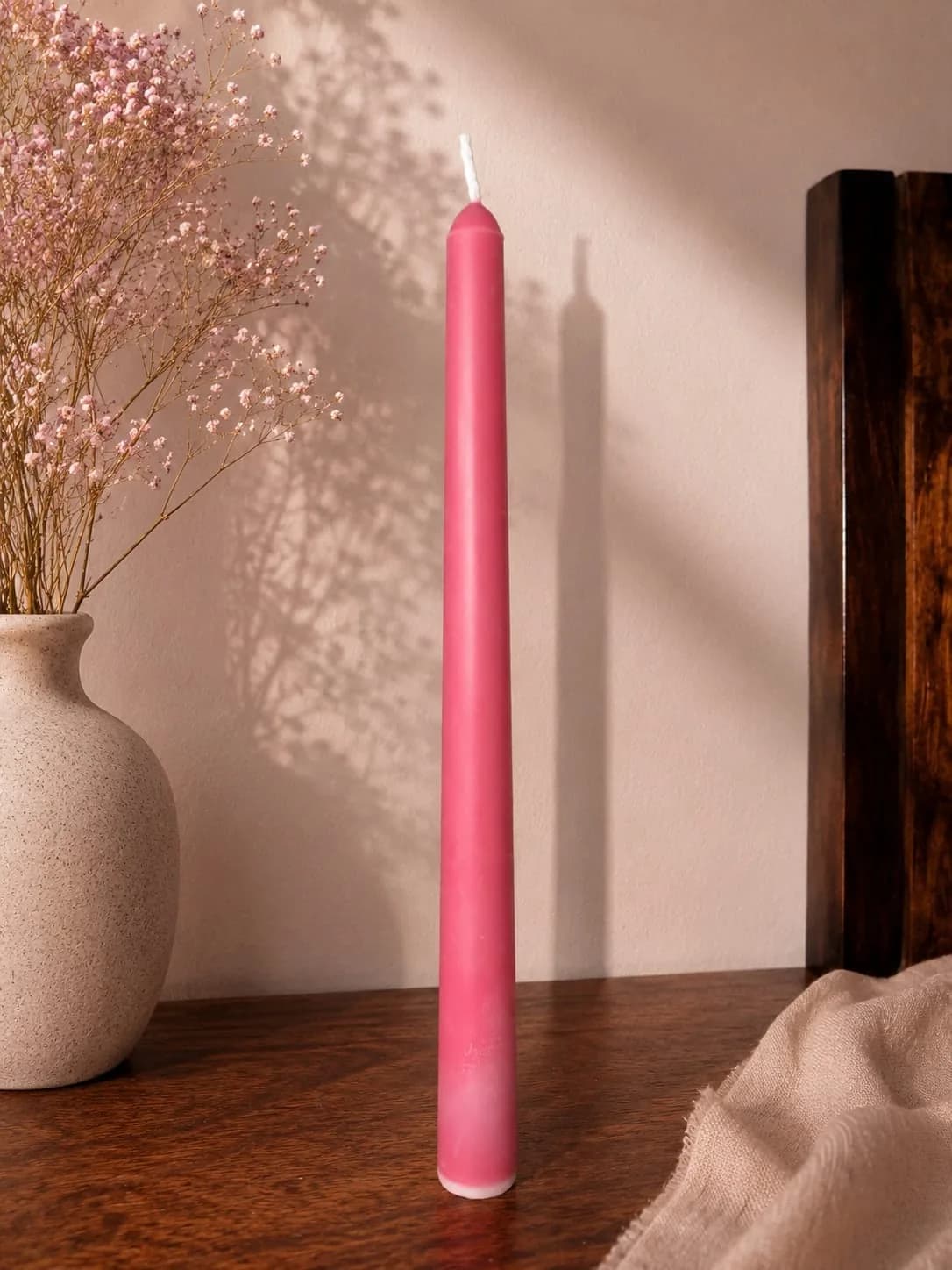 Pink taper candle standing against a sunlit wall