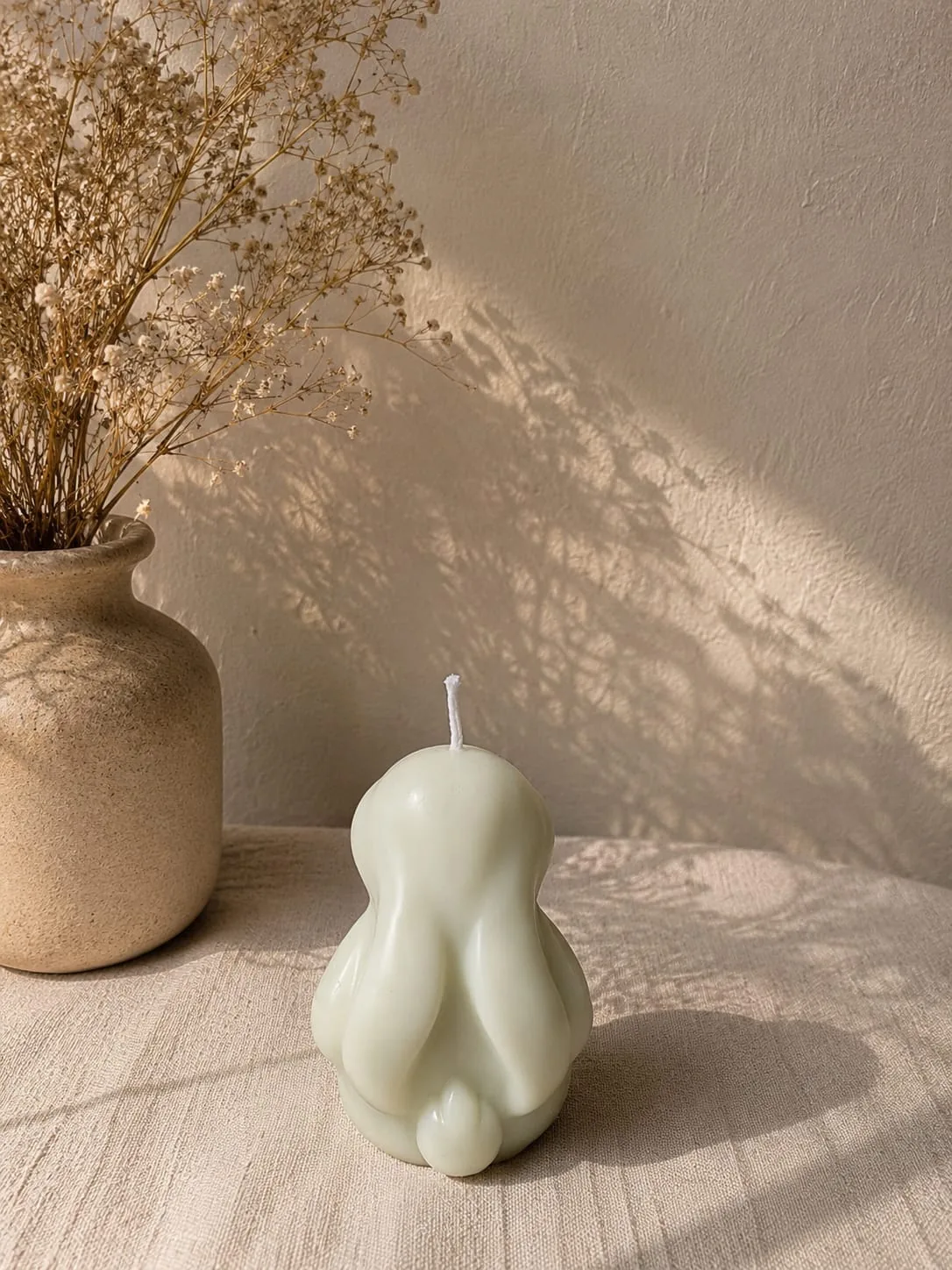 Sage green rounded candle beside a stoneware vase