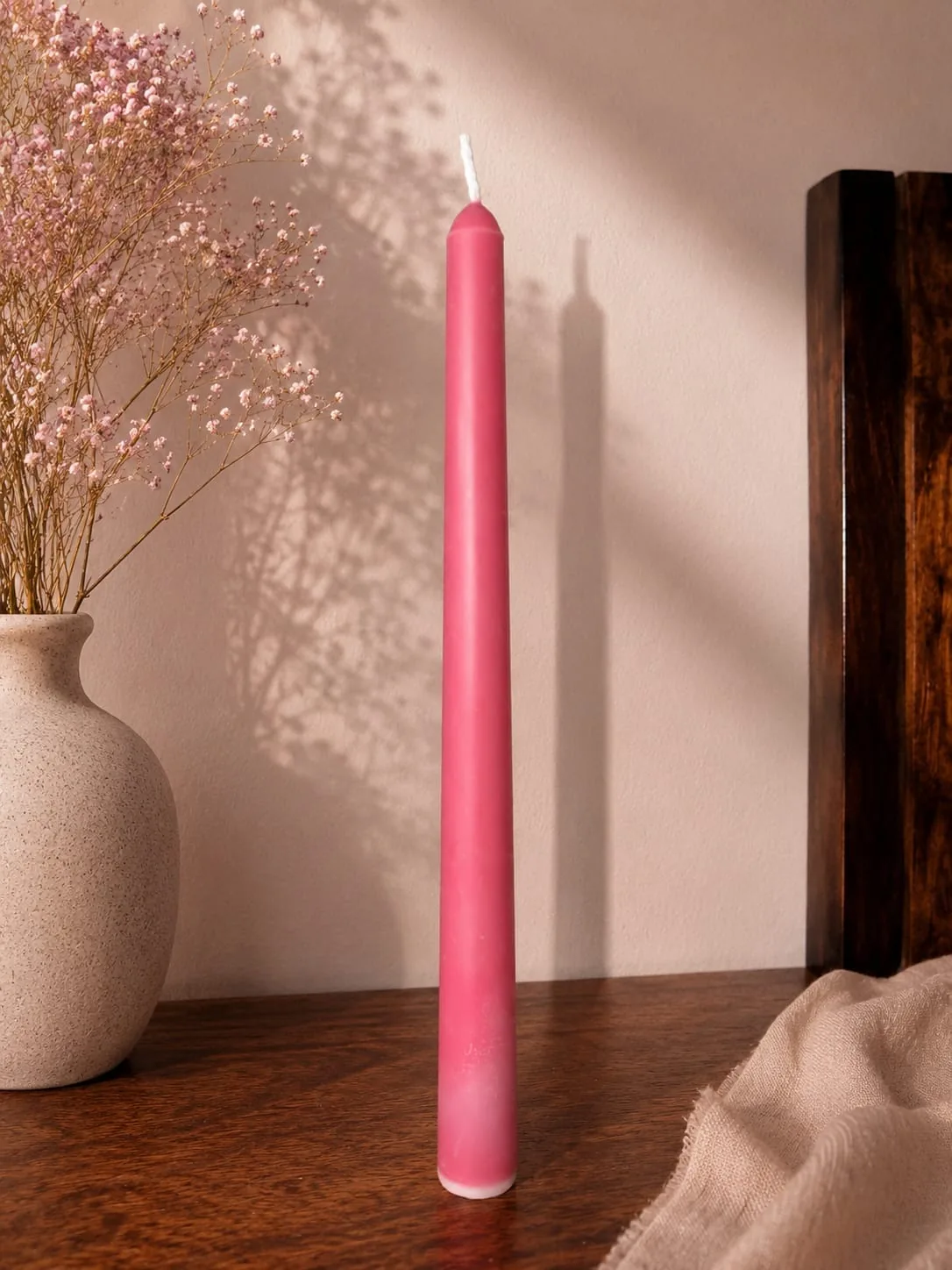 Pink taper candle standing against a sunlit wall